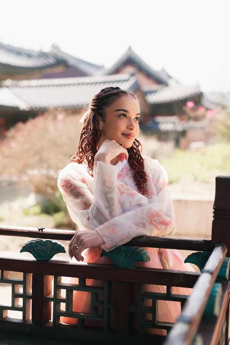 Woman in a white and pink hanbok leaning on a palace railing